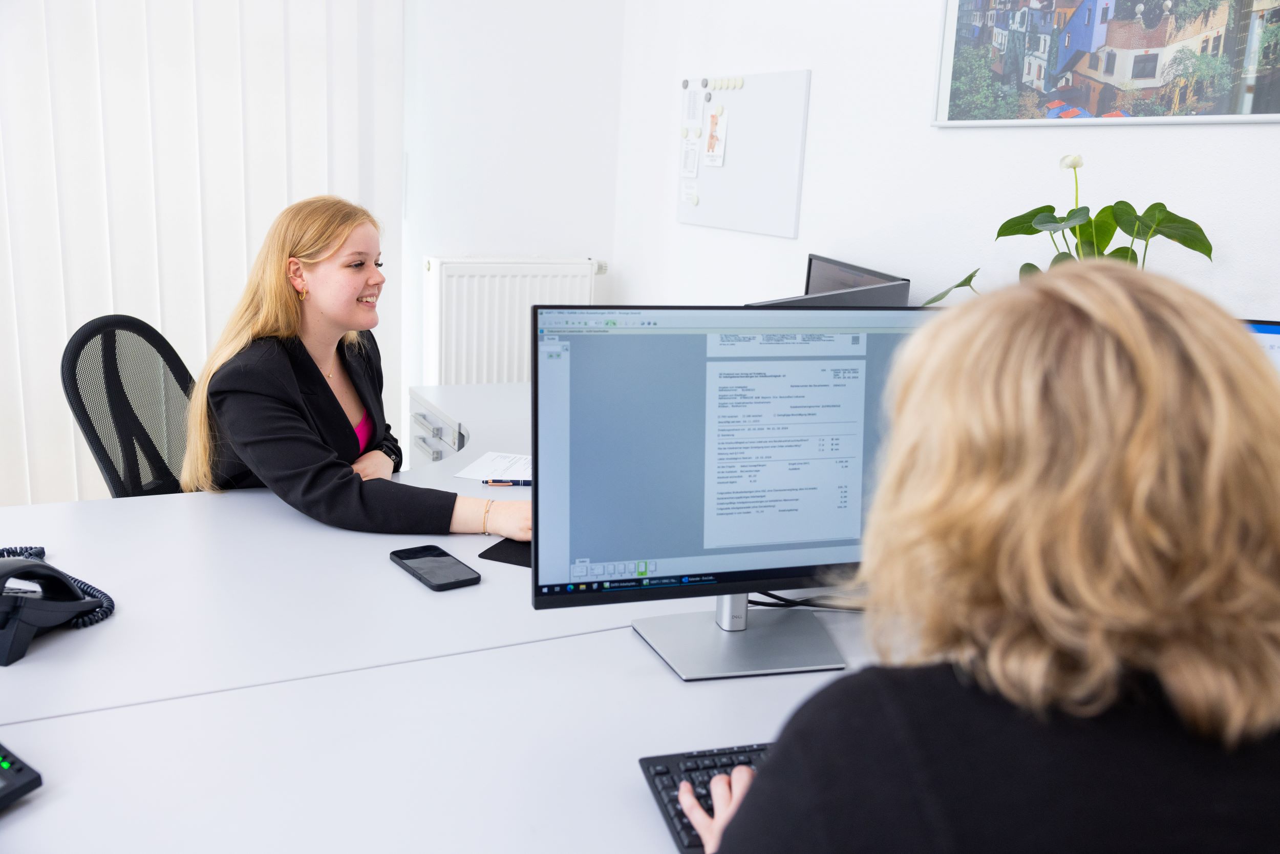 Zwei Mitarbeitende sitzen sich gegenüber und arbeiten gemeinsam am PC